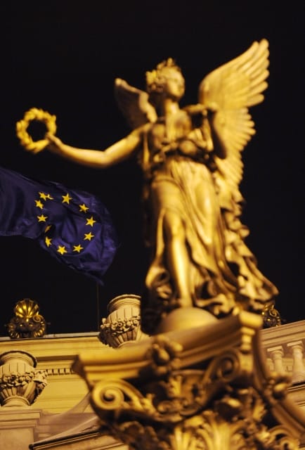Vlajka Evropské unie přes sochu na kandelábru veřejného osvětlení u budovy Rudolfina.