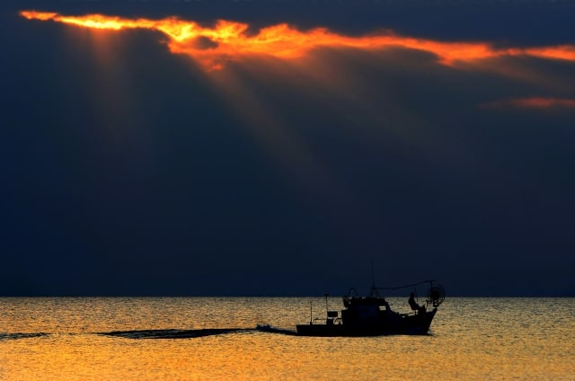 A fisherman sits at the bow of a fishing boat as the sun sets at the southeast coastal village of Xylophagou 64 kilometers (40 miles) of capital Nicosia, Cyprus, on Saturday, Feb. 10, 2007. (AP Photo/Petros Karadjias)