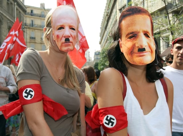 Two women wearing masks representing Interior Minister Brice Hortefeux, left, and French Immigration Minister, Eric Besson, with swastikas, demonstrate with thousands of people in Marseille, southern France, Saturday, Sept. 4, 2010, to protest against the French government's crackdown on Roma people. (AP Photo/Claude Paris) =@=